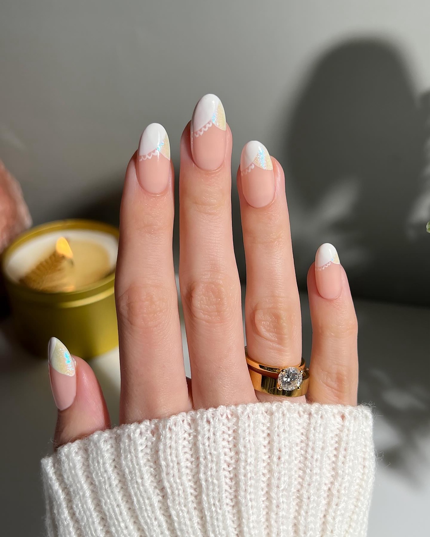 Hand met witte French manicure en subtiele nail art, naast een gouden kaars